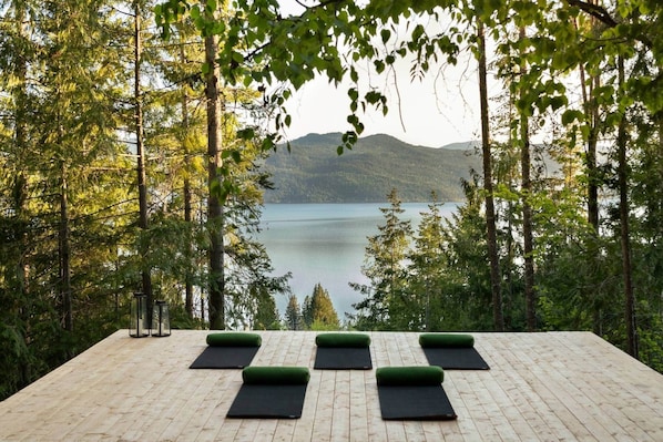 A wooden deck with yoga mats and a glass lantern, overlooking a lake and forest.