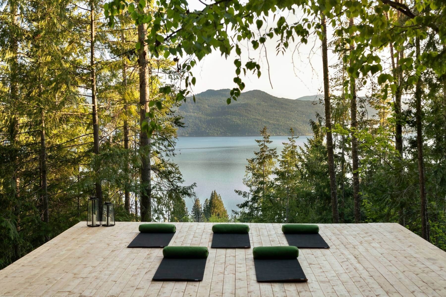 A wooden deck with yoga mats and a glass lantern, overlooking a lake and forest.
