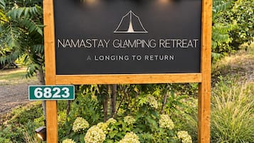 A sign for a camping retreat with a tent logo, surrounded by greenery and rocks.
