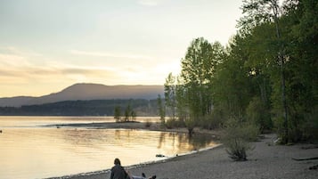 A person sitting on a log by a lake with trees and a mountain in the background.