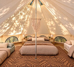 Una carpa con una cama, dos mesitas de noche y un tapiz de macramé en la pared.