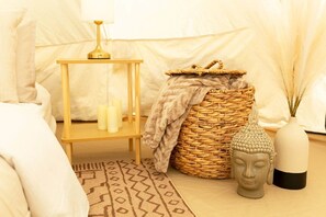 A room with a bed, a bedside table with candles, a woven basket, a Buddha statue, and a lamp.