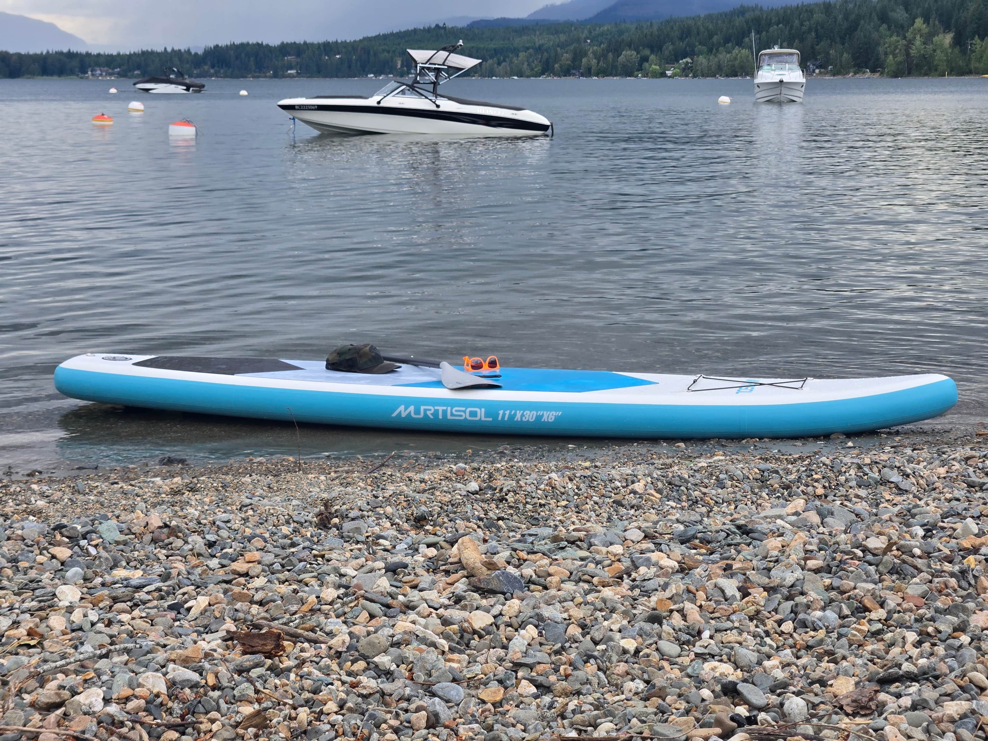 A blue inflatable raft on a pebbly shore with calm water and boats in the background.