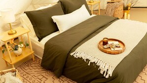 A tented room with a bed, bedside tables, a lamp, a tray with a candle, and a woven basket.