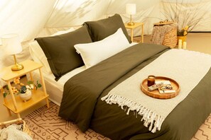 Una habitación con carpa que incluye una cama, mesitas de noche, una lámpara, una bandeja con vela y una cesta tejida.