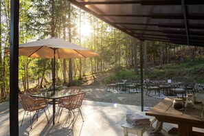 An outdoor patio with tables and chairs, surrounded by a forest.