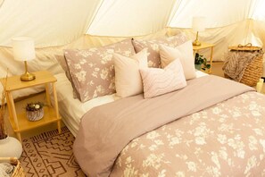 A tent-style room with a bed, pillows, a bedside table with a lamp, and a small plant.