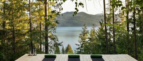 A wooden deck with yoga mats and a glass lantern, overlooking a lake and forest.