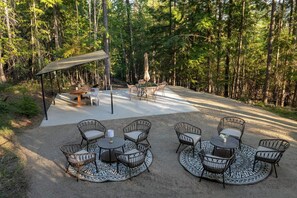 A covered outdoor seating area with tables and chairs, surrounded by a forest.
