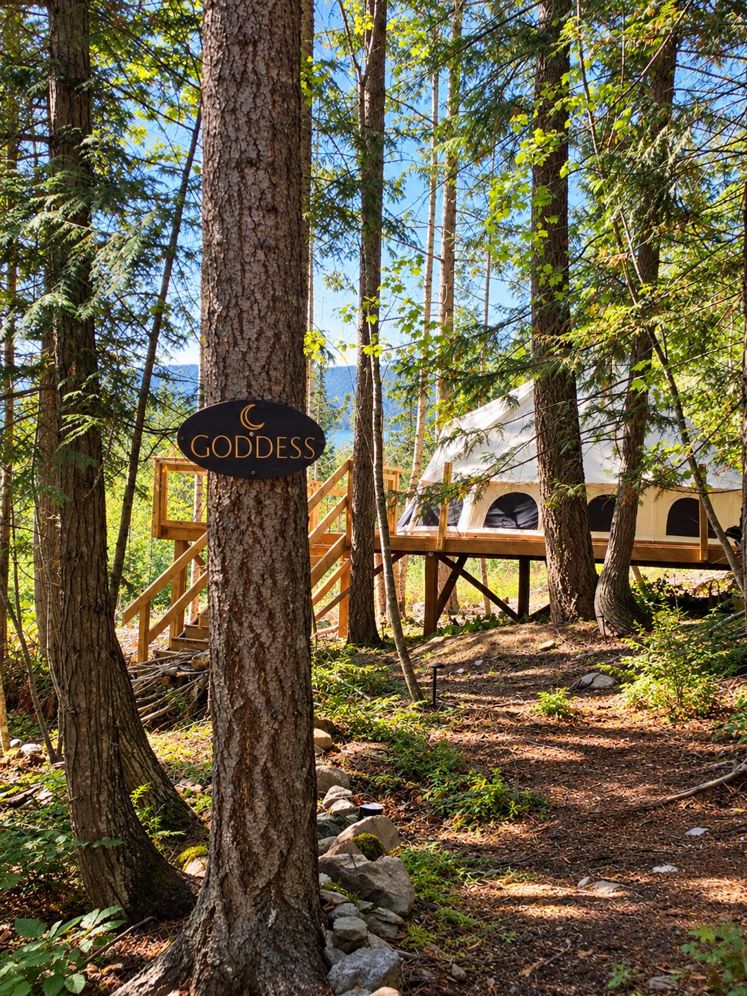 A forested area with a sign reading 'GODDESS' and a wooden structure with a view of a tent-like building.