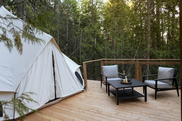 A tent on a wooden deck with two chairs and a table, surrounded by a forest.