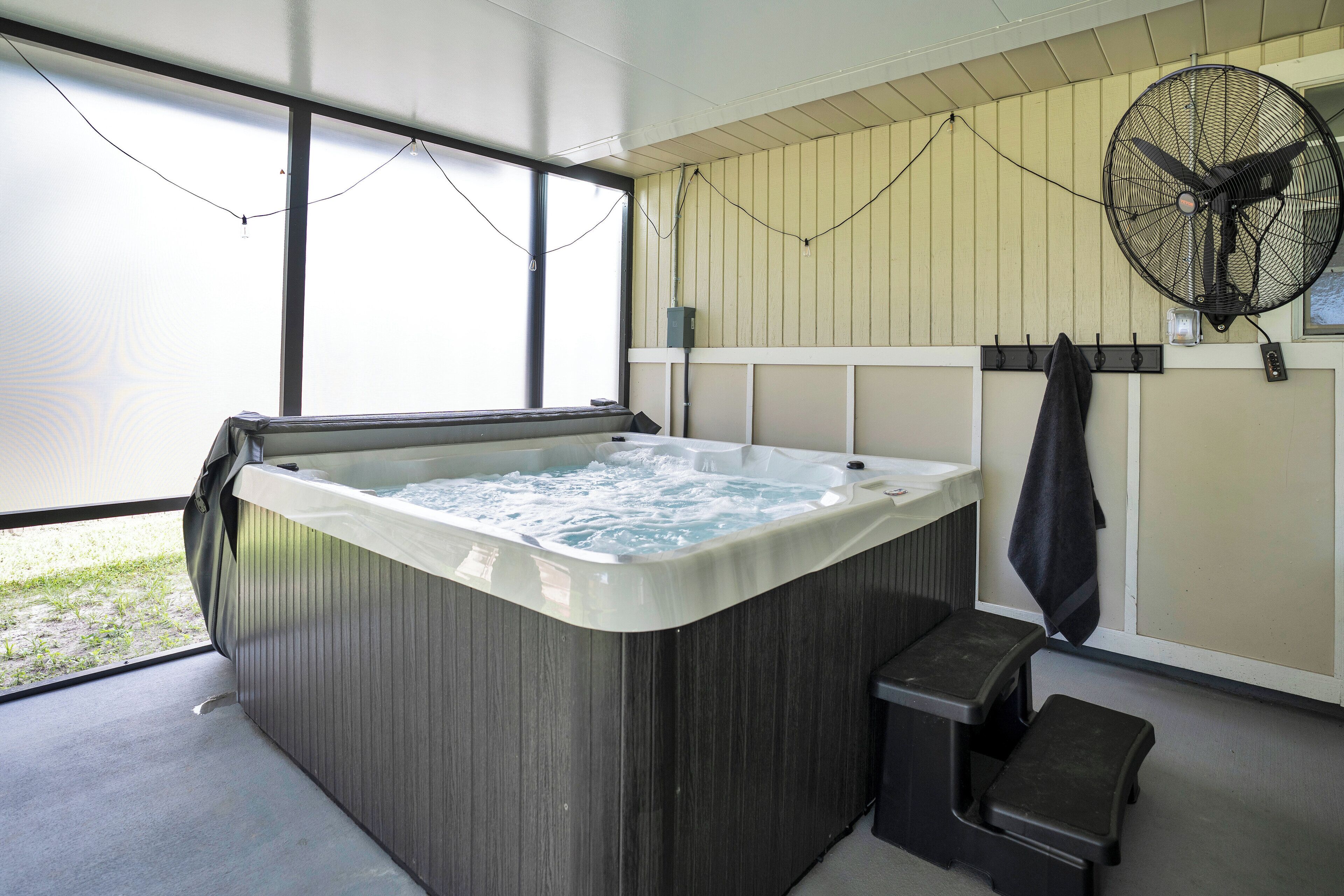A hot tub with a wooden exterior, a fan mounted on the wall, and a window providing natural light.