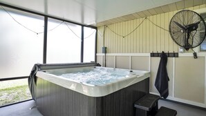 Uma banheira de hidromassagem com exterior de madeira, um ventilador fixado na parede e uma janela que oferece luz natural.