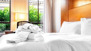 A hotel room with a bed, a window with curtains, a lamp, and a view of greenery outside. - Superhero Hotel (San Francisco)