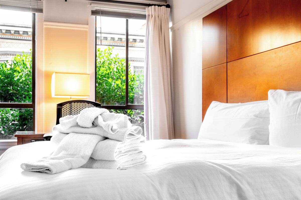 A hotel room with a bed, a window with curtains, a lamp, and a view of greenery outside.