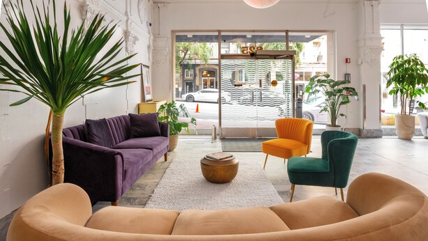 A modern lobby with a purple sofa, an orange chair, a green armchair, and a large potted plant. - Superhero Hotel (San Francisco)