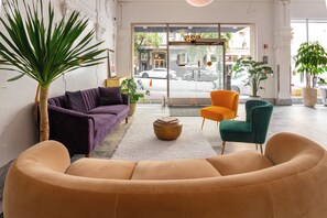 A modern lobby with a purple sofa, an orange chair, a green armchair, and a large potted plant. - Superhero Hotel (San Francisco)