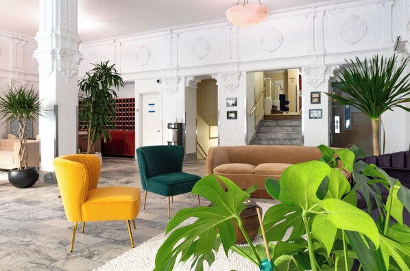 A lobby with a marble floor, a staircase, a yellow armchair, a green armchair, and a brown sofa. - Superhero Hotel (San Francisco)