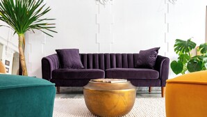 A modern living room with a purple sofa, a round gold coffee table, and a teal armchair. - Superhero Hotel (San Francisco)
