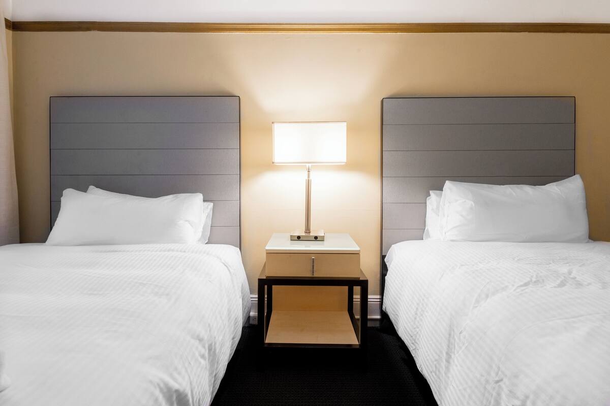 A hotel room with two beds, a nightstand with a lamp, and a wooden headboard.