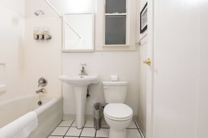 A bathroom with a bathtub, sink, toilet, and a window. - Superhero Hotel (San Francisco)