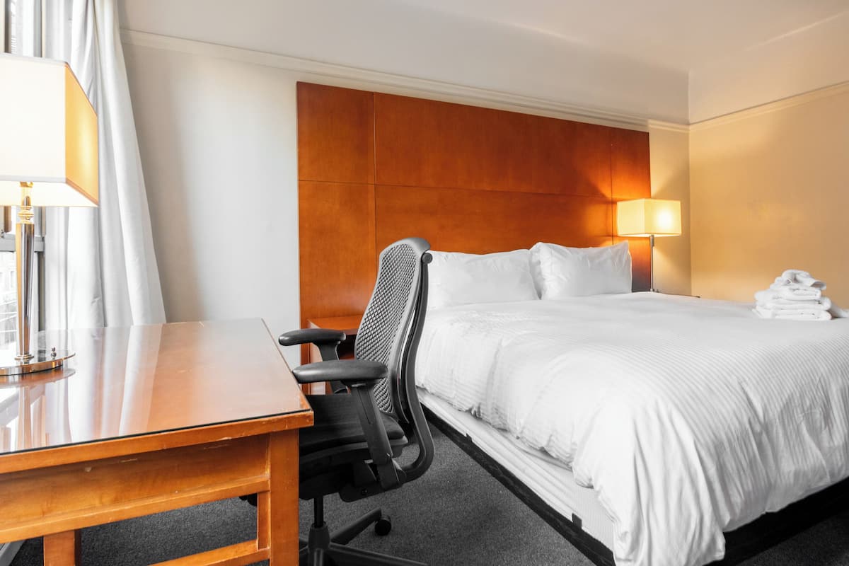 Une chambre d’hôtel avec un lit, un bureau, une chaise, une lampe et une pile de serviettes.