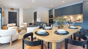 Ein modernes Wohnzimmer mit Essbereich, grauen Schränken und einer Küche mit Einbauofen und Spüle.