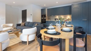 Ein modernes Wohnzimmer mit einem grauen Sofa, einem Couchtisch und einem Essbereich mit einem Holztisch, gedeckt für sechs Personen.