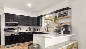 Cozinha moderna com armários pretos, eletrodomésticos de aço inoxidável, uma ilha branca com banquetas e um letreiro indicando café.