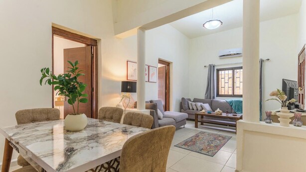 A dining area with a marble table, chairs, and a potted plant. There is a sofa and a coffee table in the background. - Daya 2BR Apartment In Batroun (Batroun)