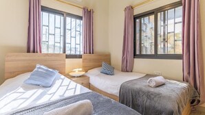 A hotel room with two beds, a nightstand, and a window with curtains. - Daya 2BR Apartment In Batroun (Batroun)