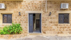 A stone building with a central doorway, two air conditioning units, and a small garden area. - Daya 2BR Apartment In Batroun (Batroun)