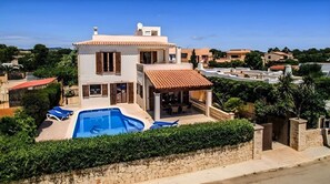A modern two-story house with a swimming pool, a covered patio, and a stone wall.