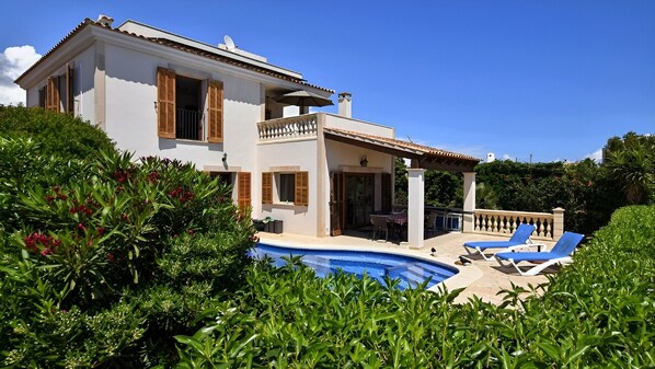 A two-story house with a swimming pool, surrounded by lush greenery.