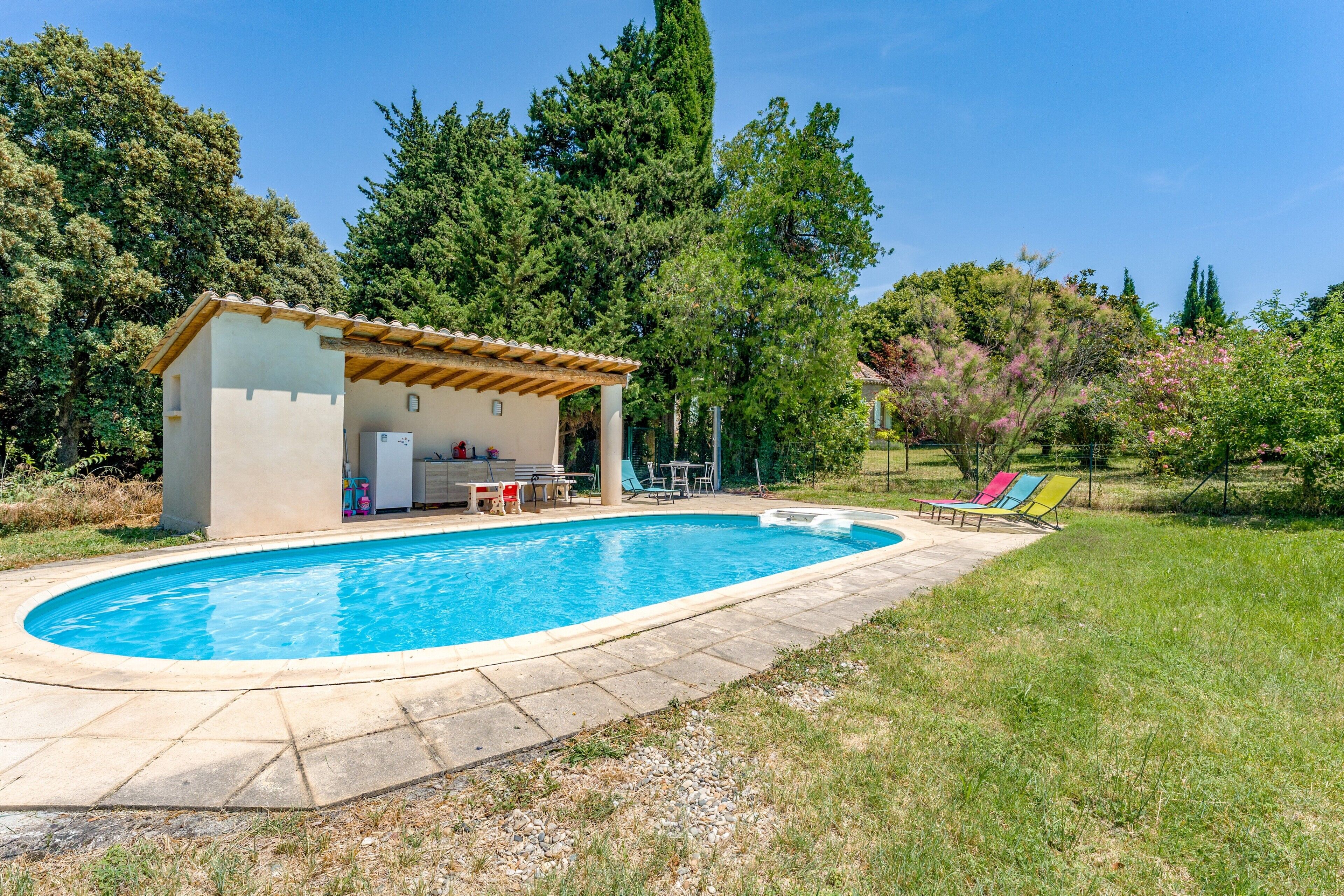 A swimming pool with a covered patio area, surrounded by trees and a grassy lawn.