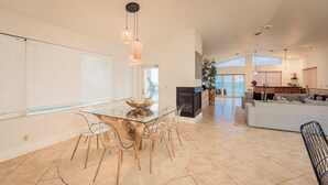 Amplia sala de estar con mesa de comedor de vidrio, sillas transparentes, chimenea, sofá y vista al océano.