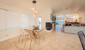 A spacious living area with a glass dining table, clear chairs, a fireplace, a sofa, and a view of the ocean. - Oceanfront Luxury Villa 5BR/4BA Beach Access (Hollywood)