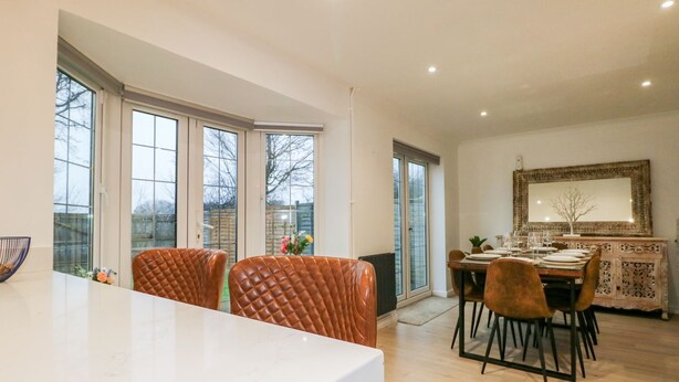 A modern dining area with a large table, leather chairs, and a view through large windows. - Number 5 (Chichester)