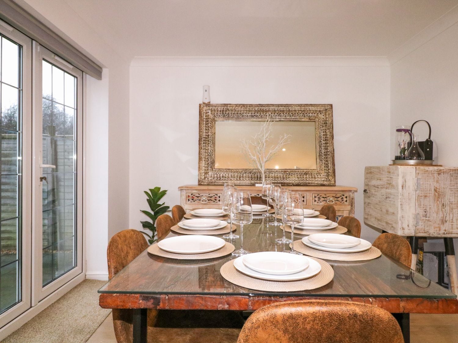 A dining area with a glass table set for six, surrounded by upholstered chairs.