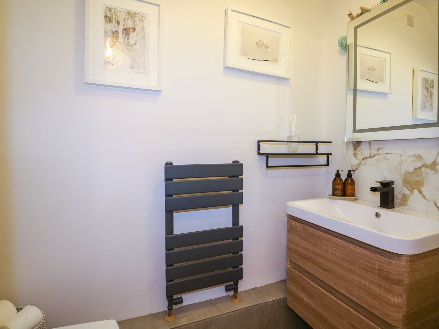 Une salle de bain moderne avec un porte-serviettes noir, un lavabo blanc et un pare-éclaboussures en marbre.