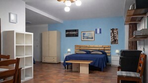 A bedroom with a bed, a desk, a chair, a wardrobe, and a shelf with items. - Hotiday Monopoli Collina (Monopoli)