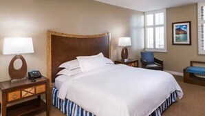 A hotel room with a large bed, two bedside tables with lamps, a chair, and a window with blinds.