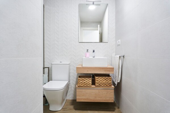 Un baño con inodoro, lavamanos, espejo y toallero.