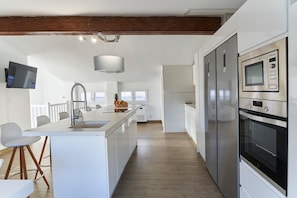 A modern kitchen with a central island, stainless steel appliances, and a wooden ceiling beam. - Casa Rural Pico Mágina: Your Comfortable Home Away from Home (Albanchez de Mágina)