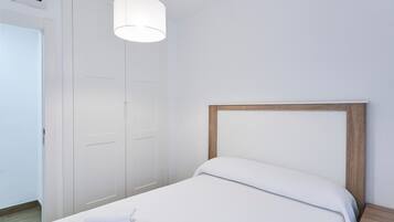 Et hotelværelse med en seng, et træhovedgærde, en hvid væg, en dør og en hængende lysarmatur.