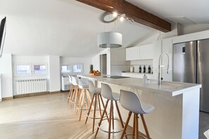 Una cocina moderna con una isla central, taburetes de bar, un refrigerador de acero inoxidable y un ventanal grande.