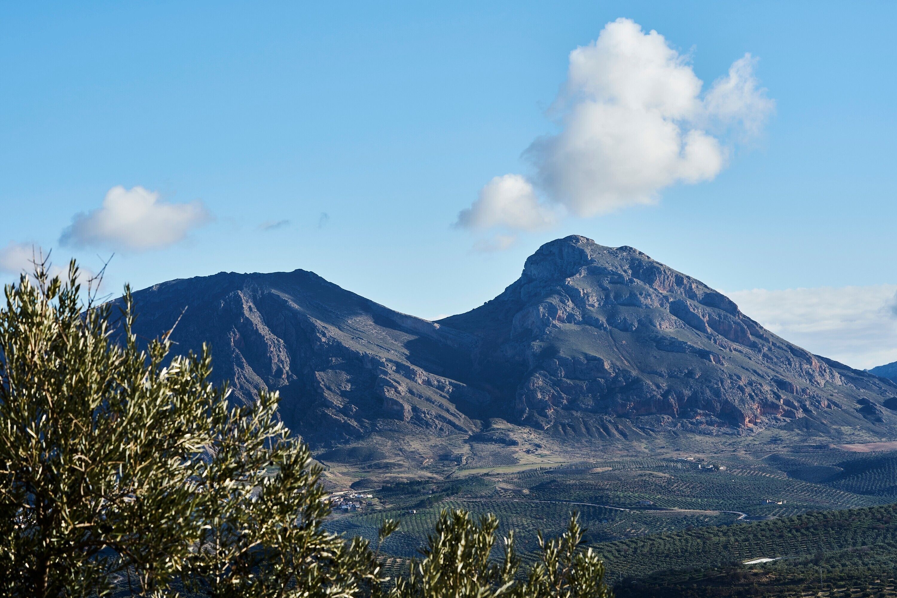 Un paisaje montañoso con un pico destacado, un valle con campos en terrazas y un cielo despejado.