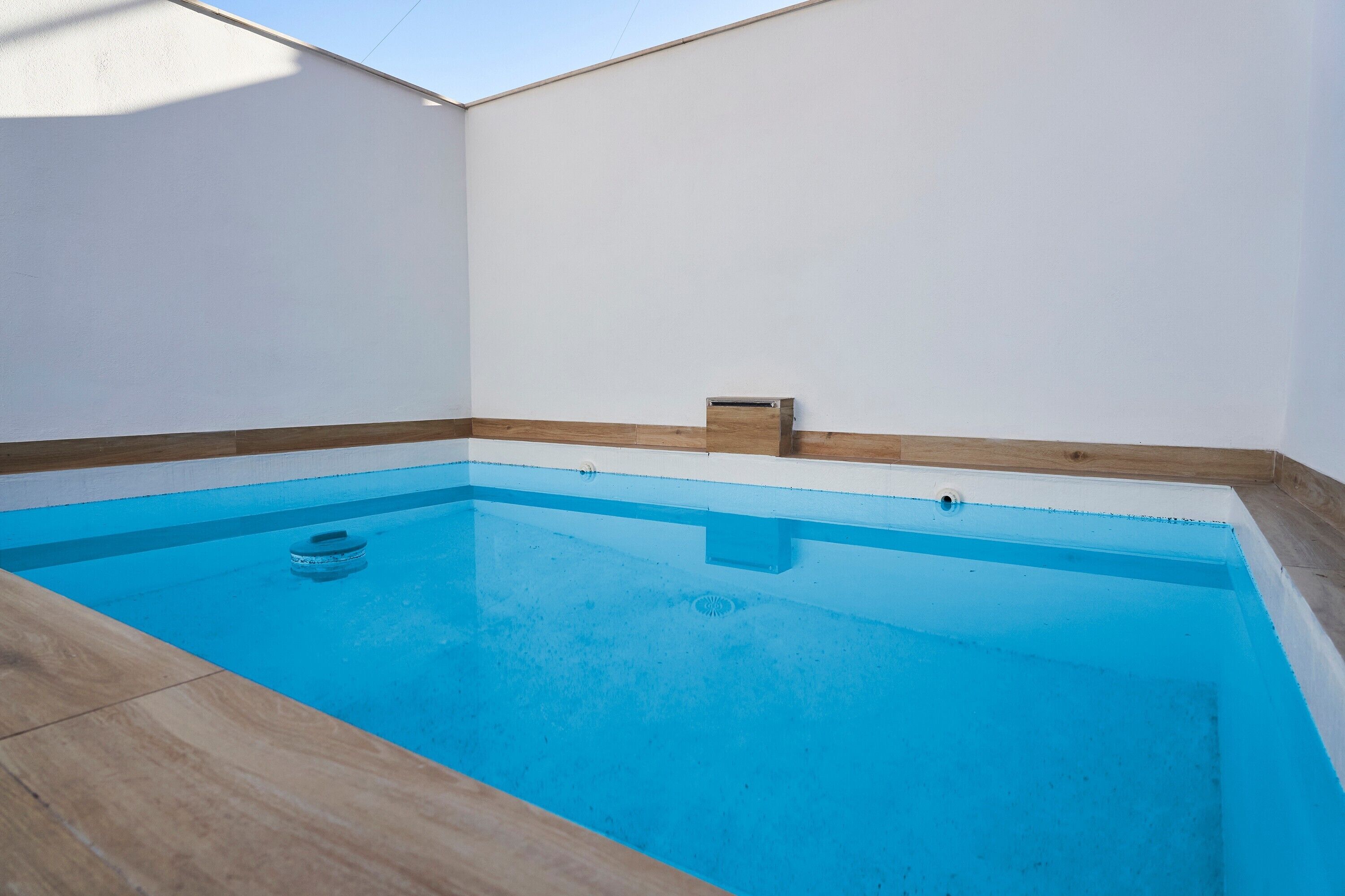 Una piscina rectangular con una cubierta de madera alrededor.