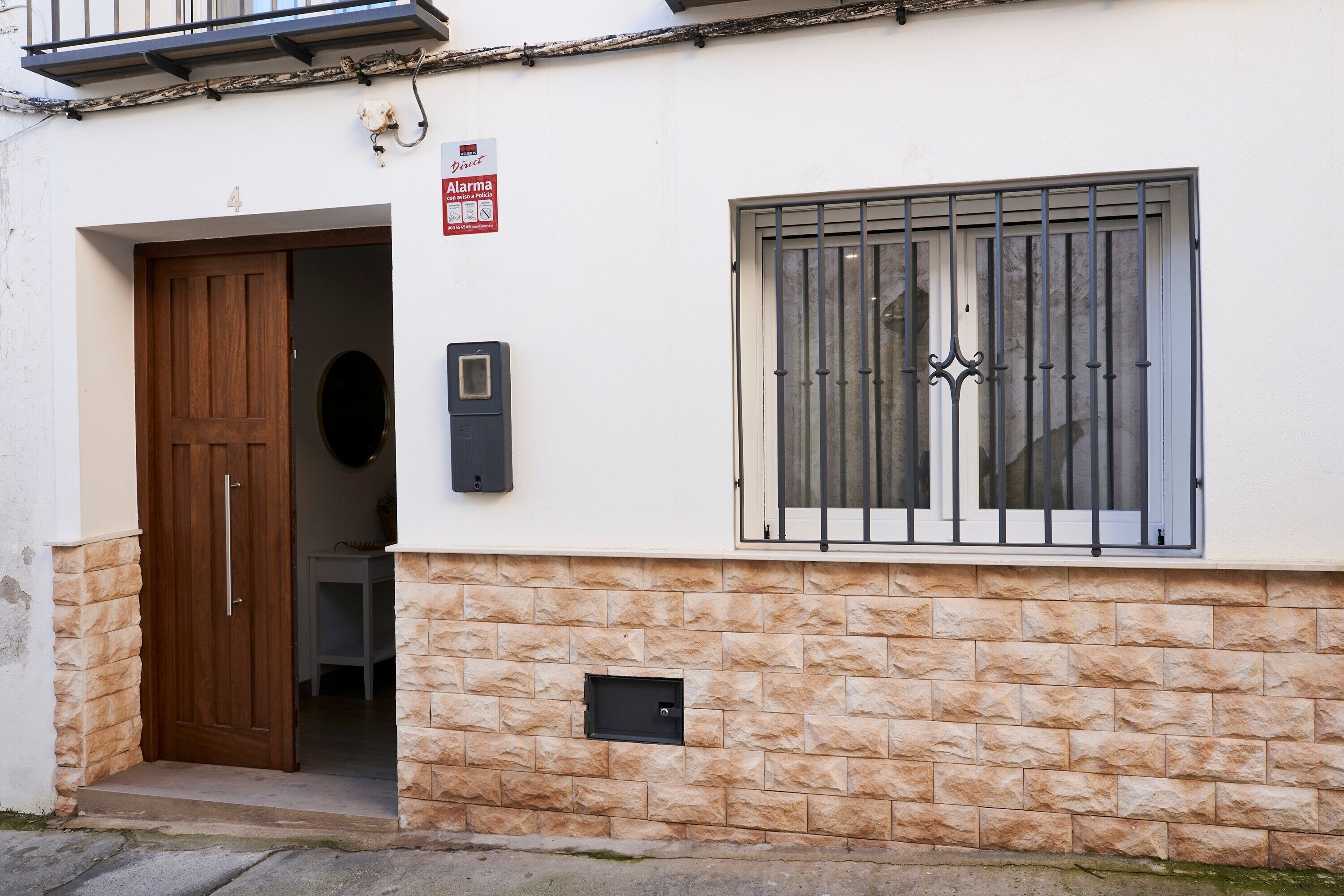 Un edificio con fachada de piedra, una puerta de madera, una ventana con barrotes y un letrero que indica un sistema de alarma.