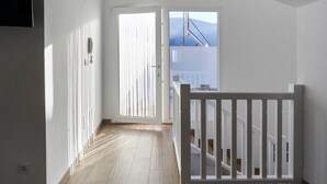 Un couloir doté d’un plancher en bois, de murs blancs, d’une porte blanche et offrant une vue sur un balcon avec une balustrade.